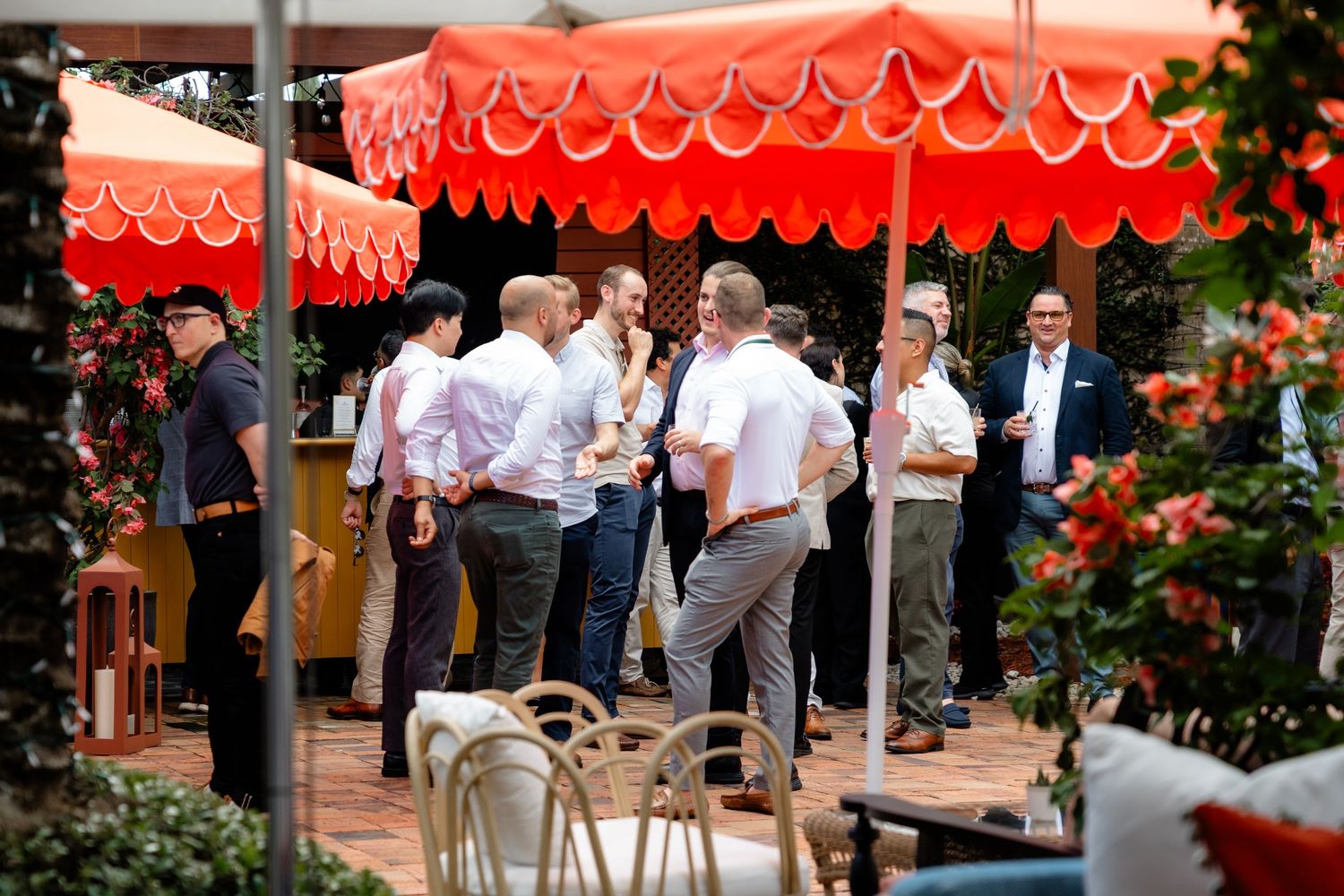 Group of men socializing outdoors under vibrant red scalloped umbrellas at an upscale garden party event.
