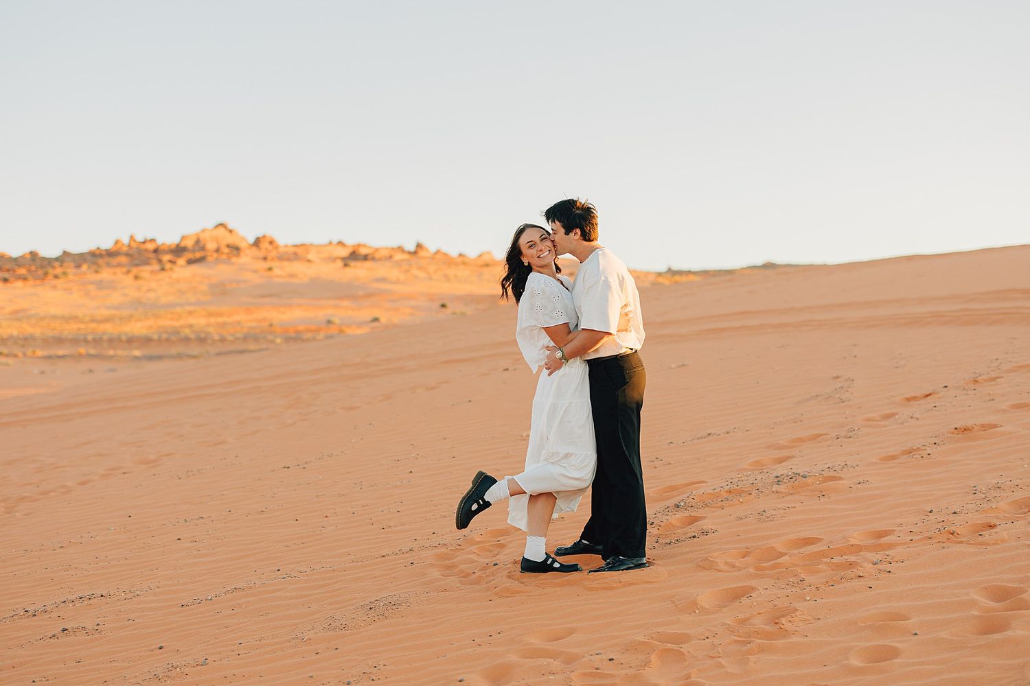 Couple sharing a romantic kiss on red sand desert dunes at golden hour sunset.