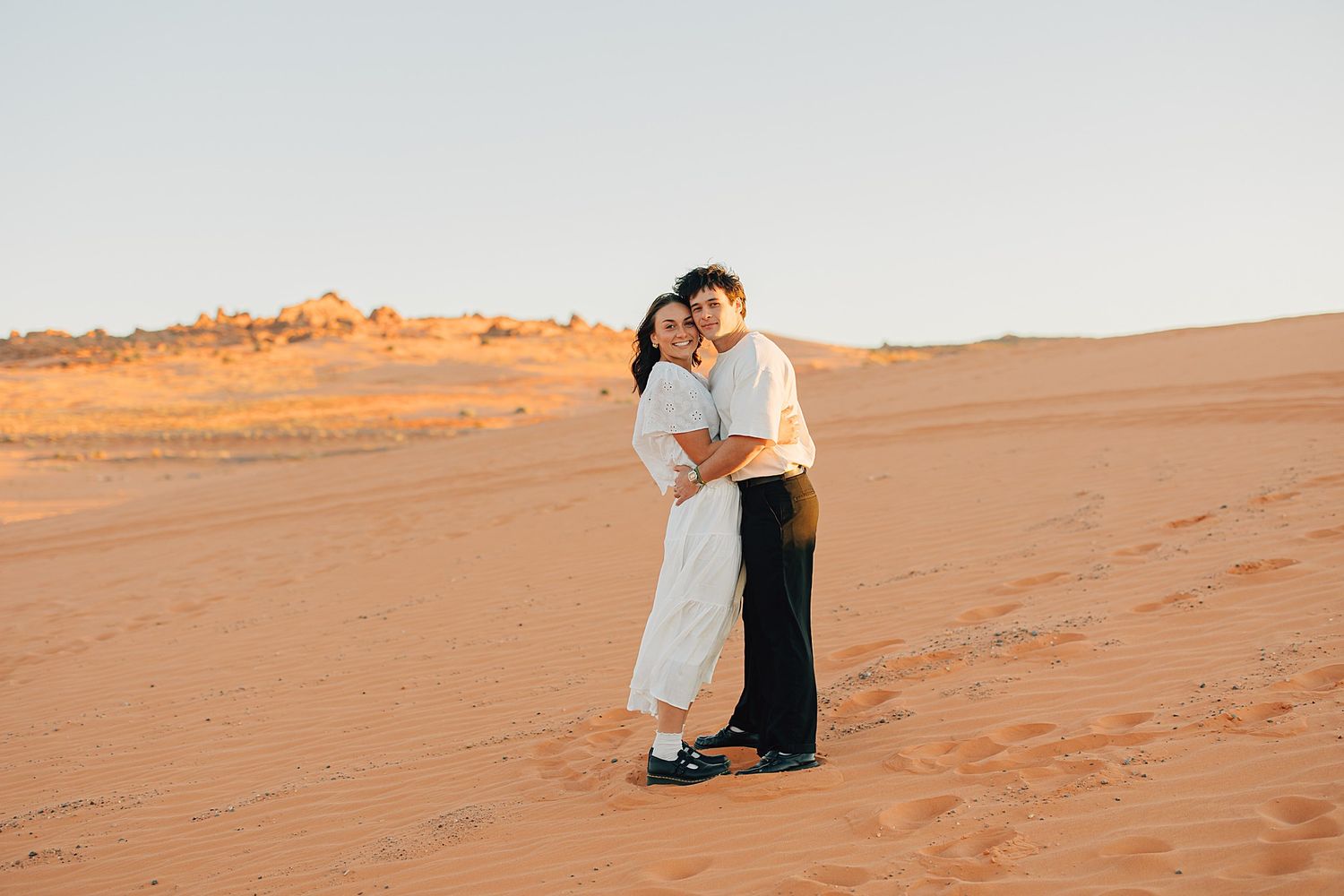 Romantic couple hugging on red sand dunes in the desert during a warm sunset.