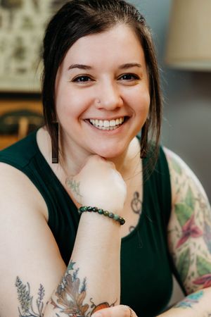 Close-up of a smiling woman with tattoos and a beaded bracelet wearing a green sleeveless top.