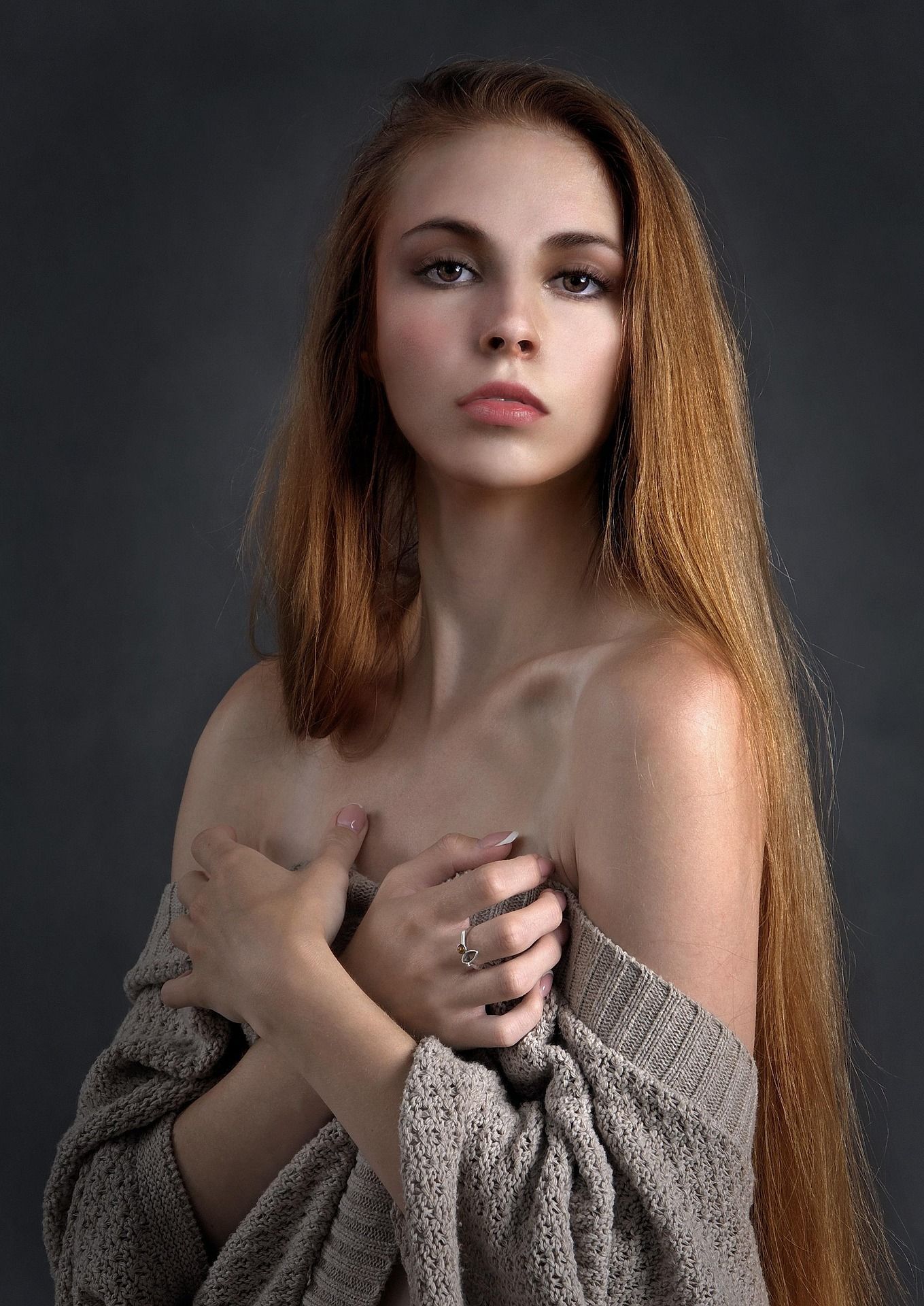 Jeune femme aux longs cheveux auburn tenant un pull en maille, portrait sur fond sombre