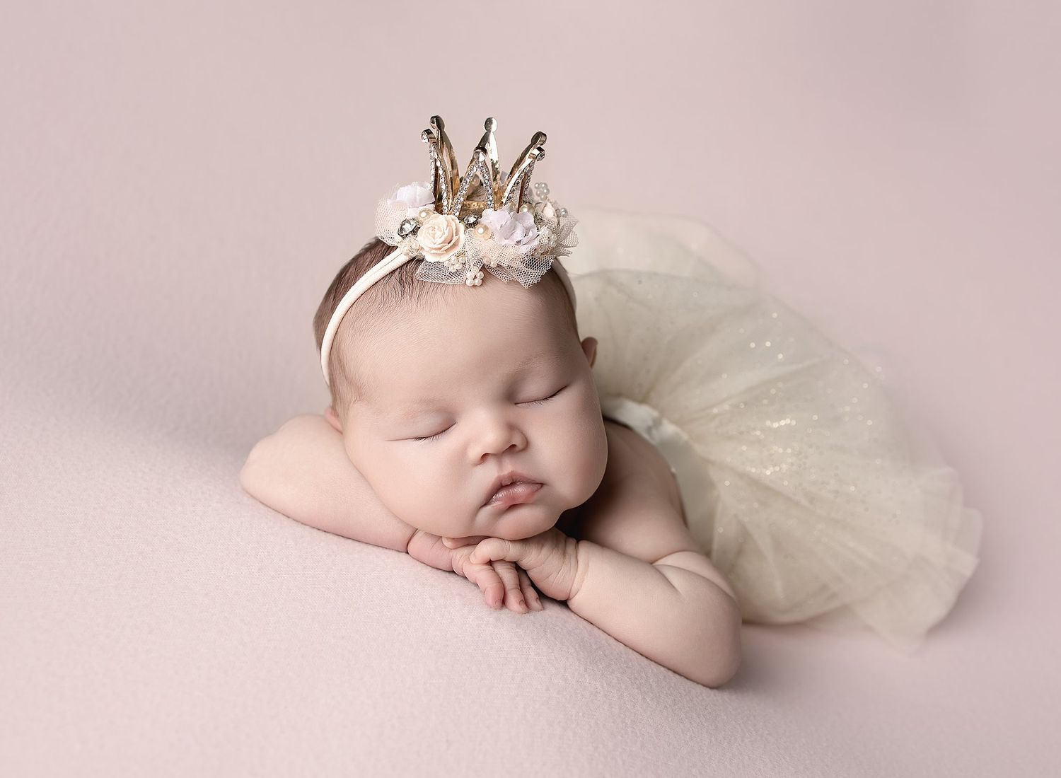 Newborn girl posed on pink with a tutu and princess tiara headband.