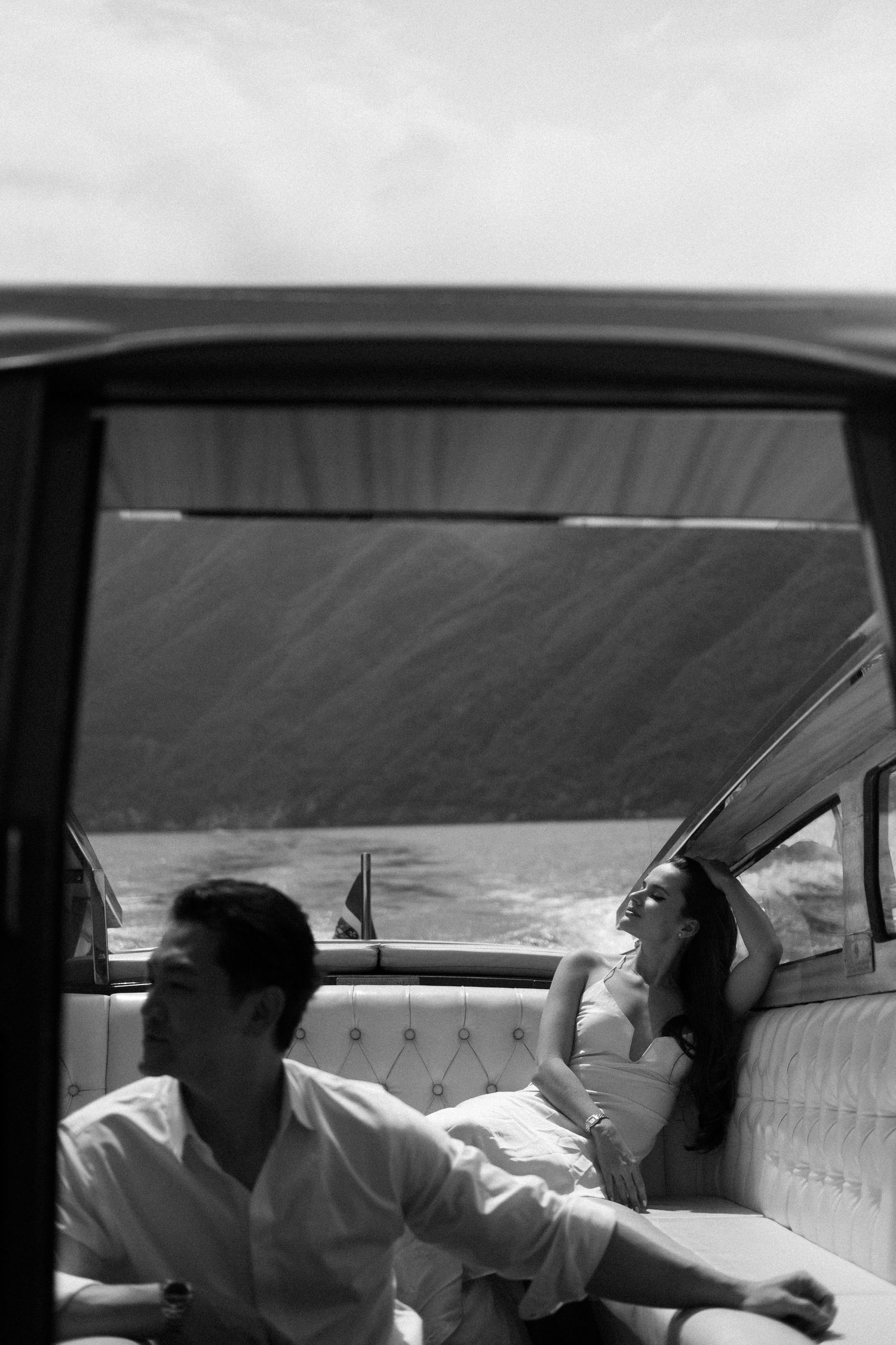 Black and white photo of a couple relaxing in a vintage boat, with water visible through the open window.