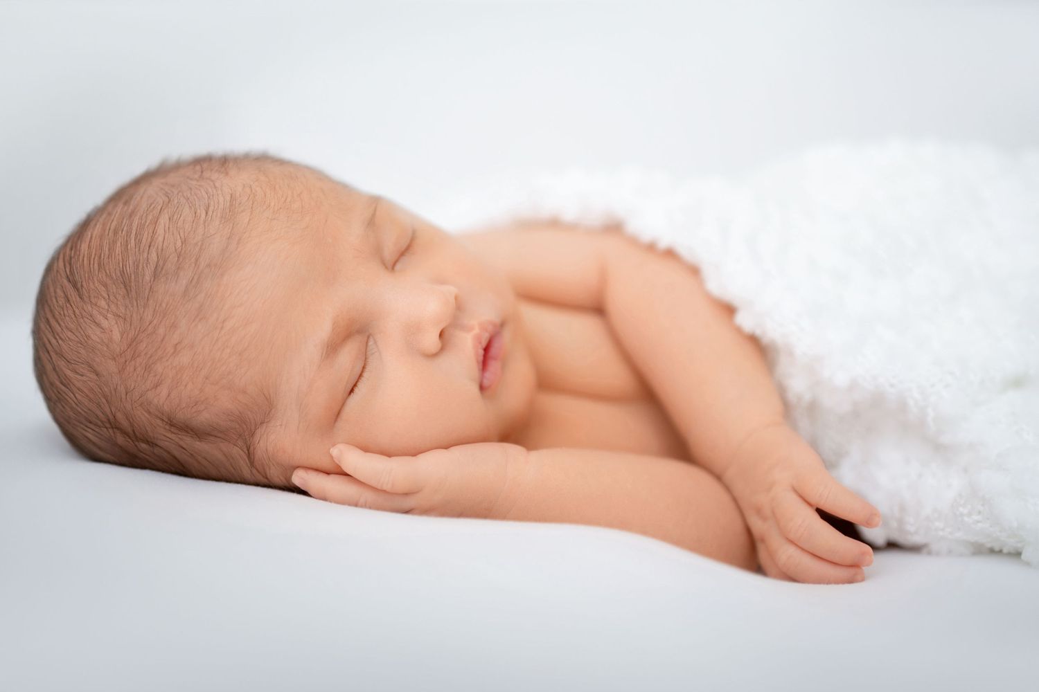 Sleeping newborn baby wrapped in a soft white blanket during studio newborn photography session in Winchester, VA