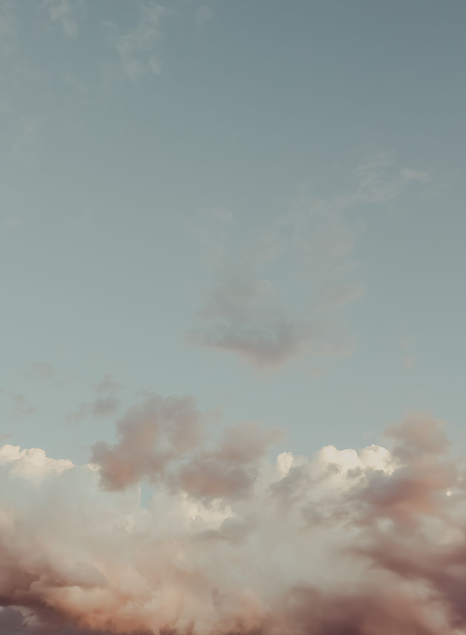 Soft pastel sky with fluffy pink and white clouds at sunset, creating a dreamy atmospheric background.