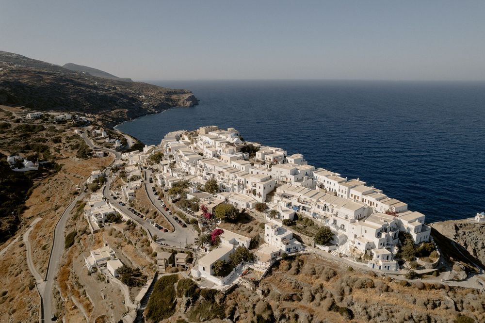 Aerial view of white-washed Greek village perched on rocky cliffs above the sea.