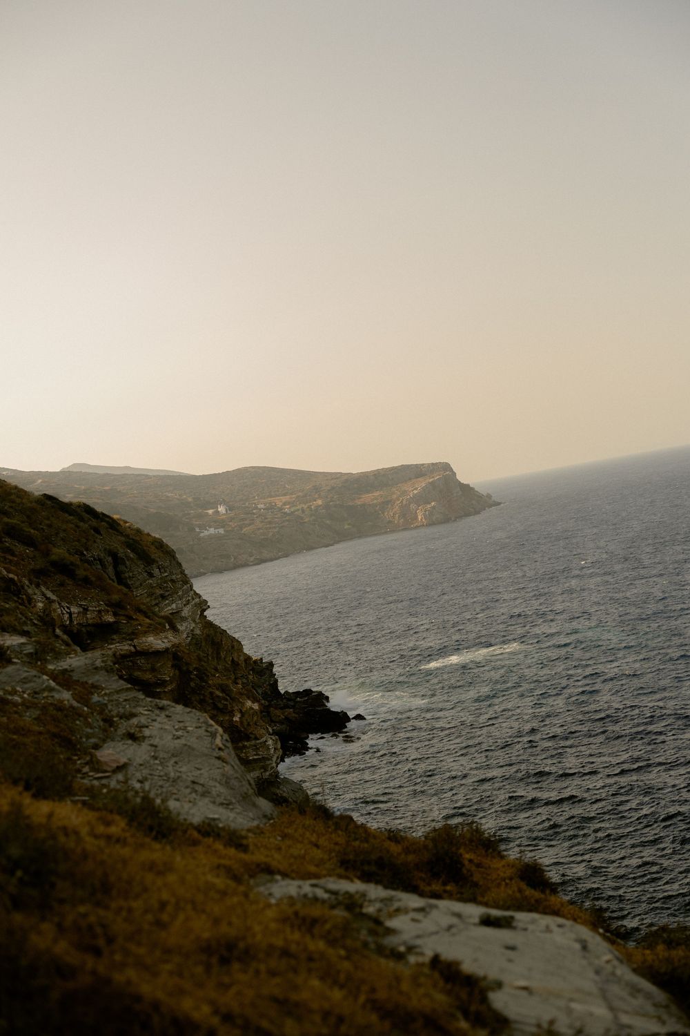 Scenic coastal cliffside view at sunset with rocky hills meeting the calm sea.