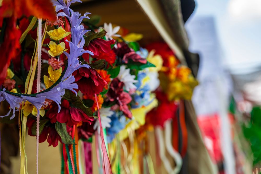 Colorful handmade flower wreaths with ribbons displayed at a festive market stall.