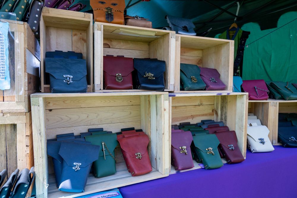 Colorful leather satchel bags displayed in wooden crate shelves at a market stall, featuring various sizes and colors.