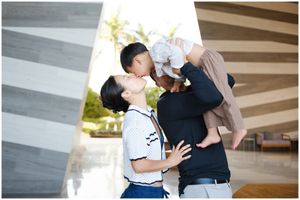destination family photographer Mexico, Asian family portrait outdoors, parents kissing baby near modern architecture columns.
