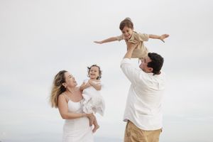 Mexico beach family photographer, parents lifting children outdoors, candid family moment against bright sky.