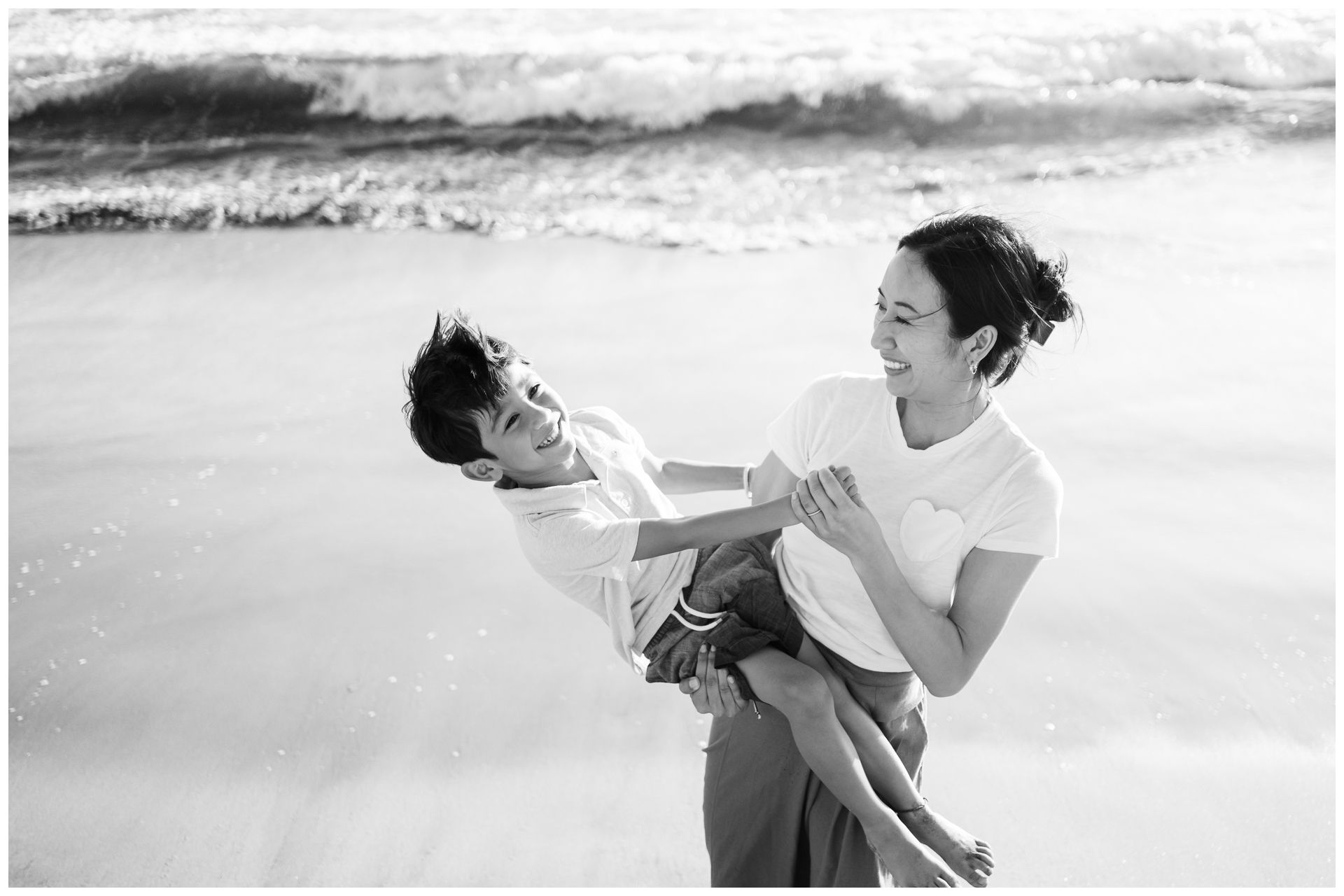 Punta Mita family photography session, woman lifting laughing child on beach, black and white ocean candid moment.