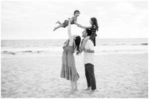 Puerto Vallarta family photographer, joyful family lifting child on beach, black and white candid ocean session.