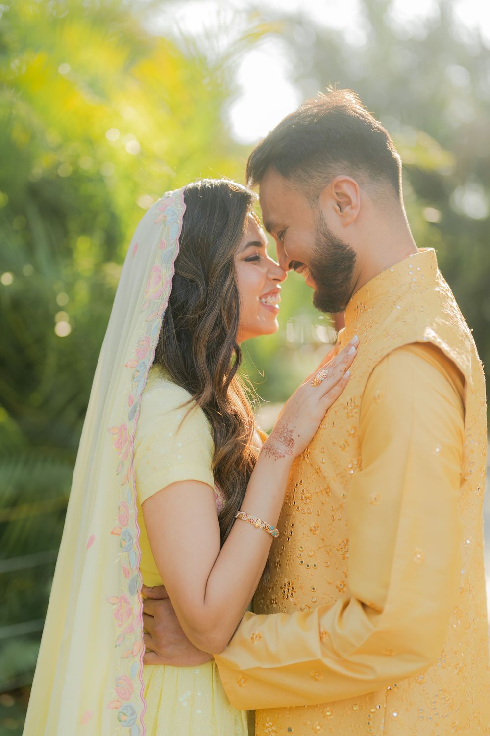 Romantic couple in yellow Indian attire sharing an intimate moment outdoors in golden sunlight.