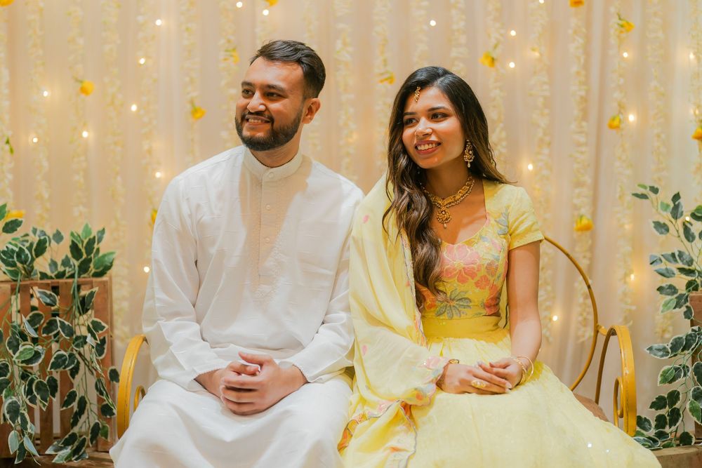 Couple in yellow and white traditional South Asian attire sitting together against a fairy light backdrop.