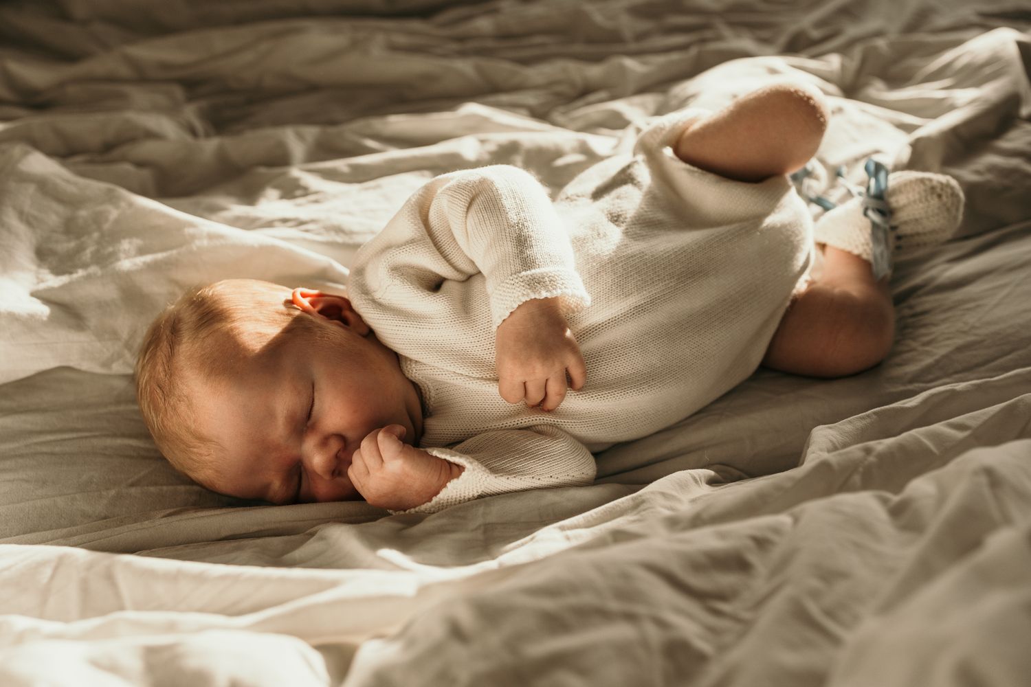 Baby feet peek out from soft white bedding while resting on a cozy bed.