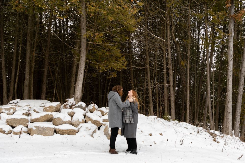 a couple admiring one another on a snowy day- with lots of trees and rocks around them
