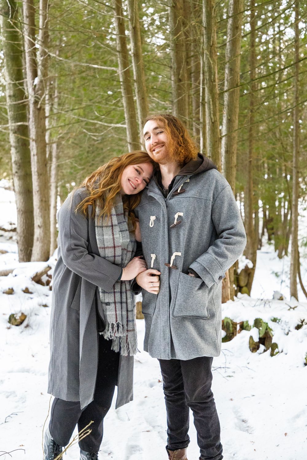 A couple in the winter forrest with the woman leaning on her mans shoulders