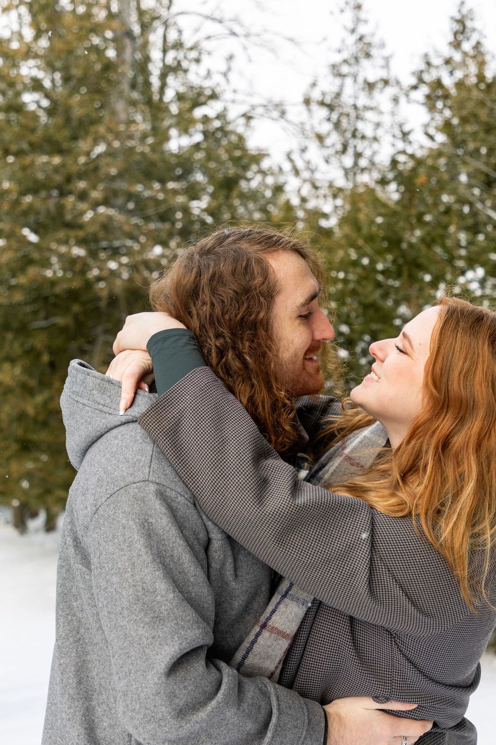 a couple admiring one another on a snowy day with the girls hands wrapped around his neck, leaned in