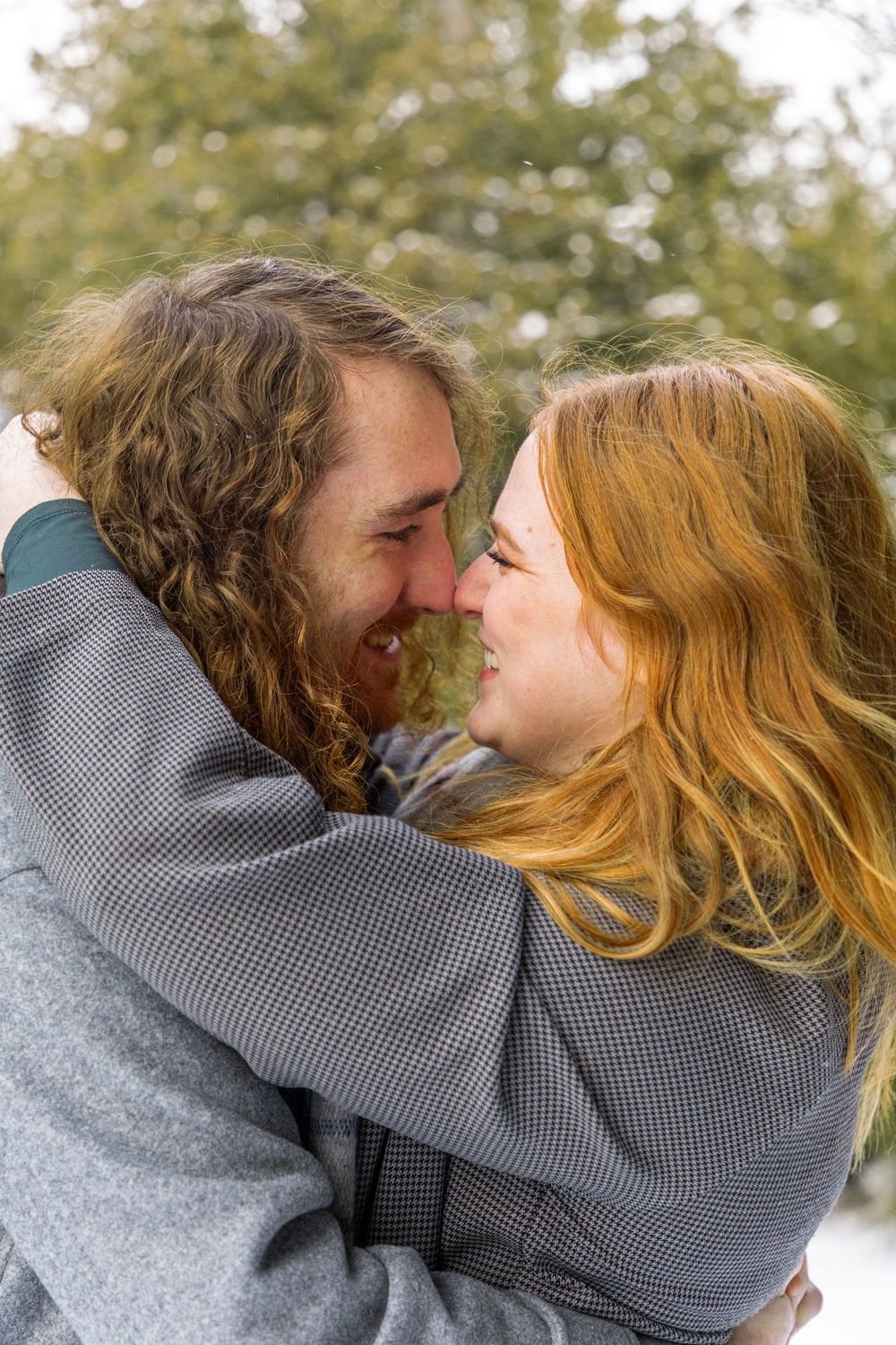 a couple admiring one another on a snowy day with the girls hands wrapped around his neck, leaned in nose to nose.