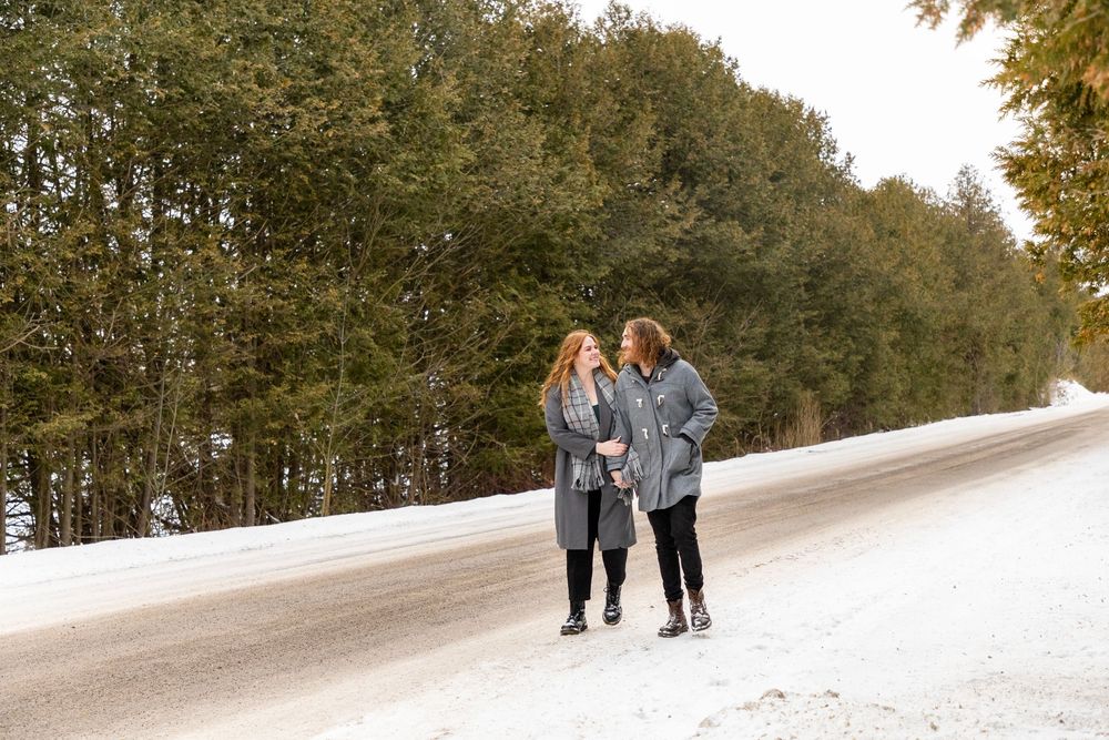 a couple admiring one another on a snowy day, walking down a snowy road holding arms