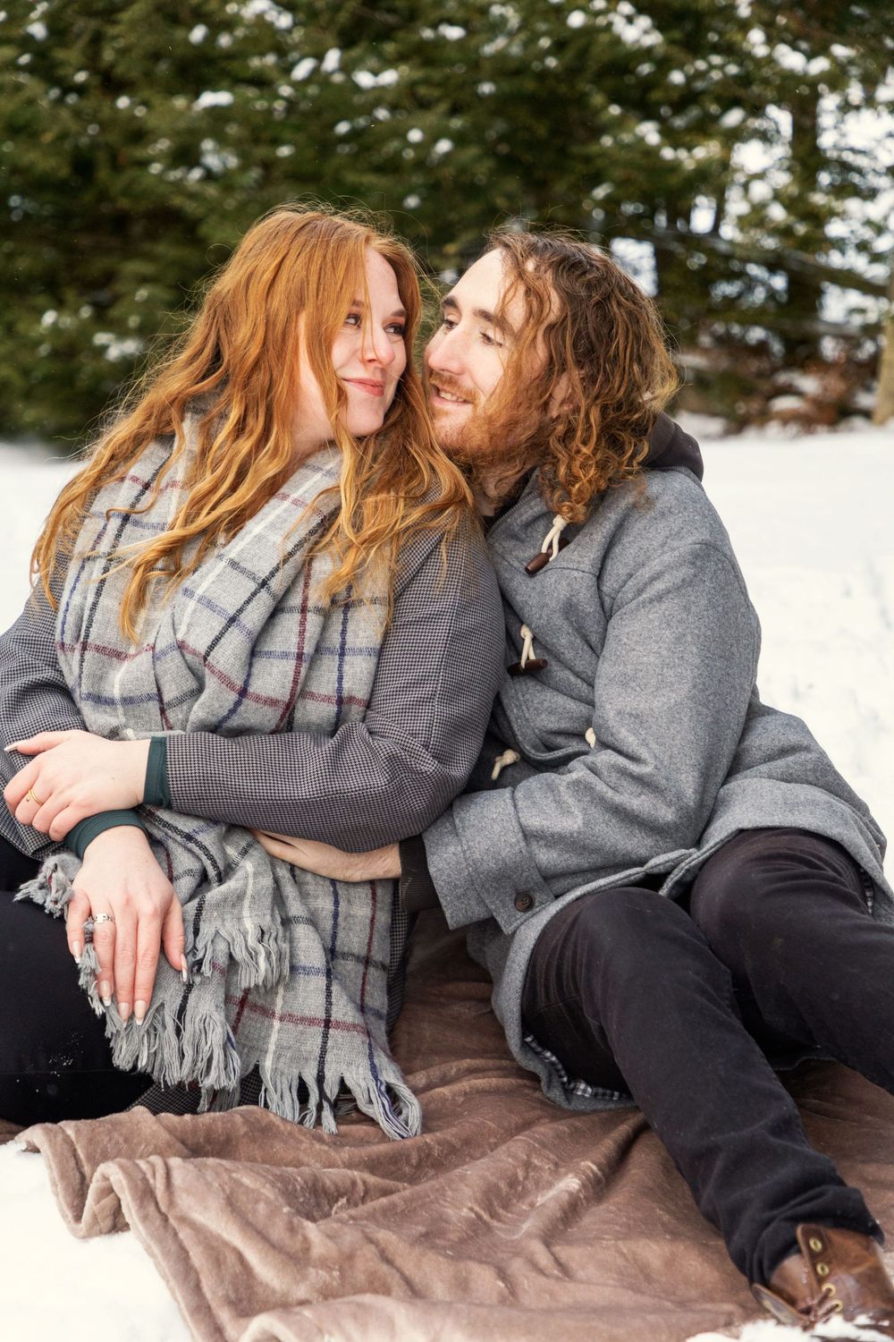 A couple cuddling in the snow on a blanket looking at each other