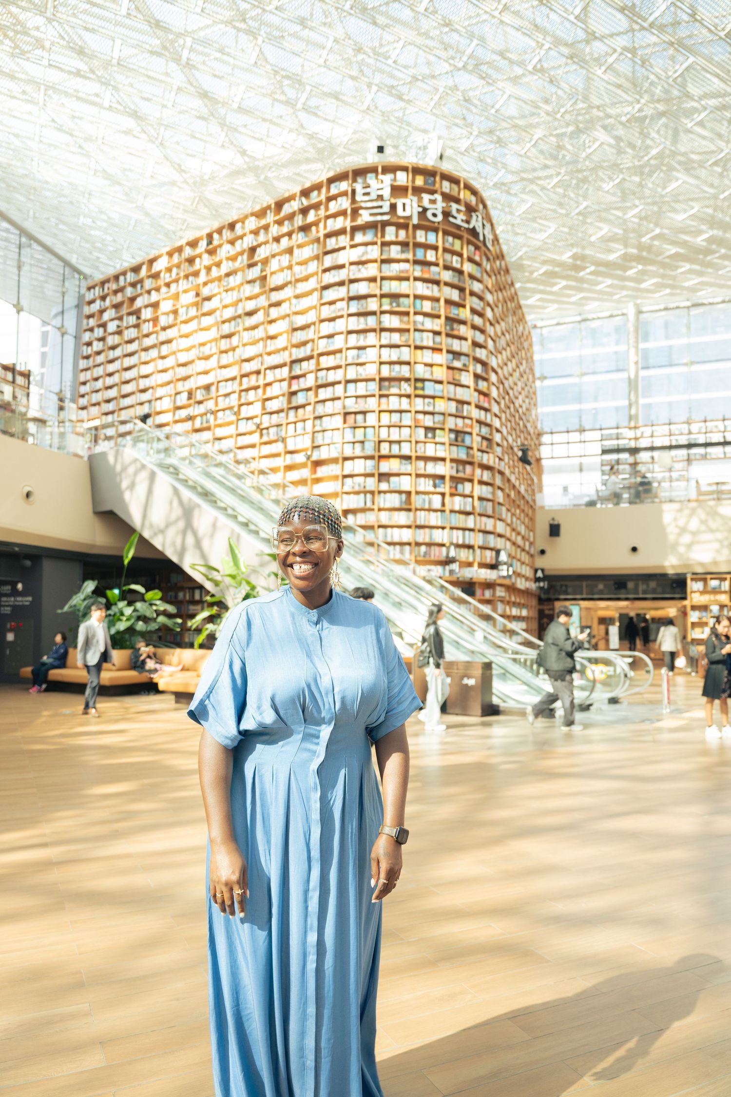 Person wearing light blue dress stands in modern building interior with curved brick wall and geometric ceiling design.