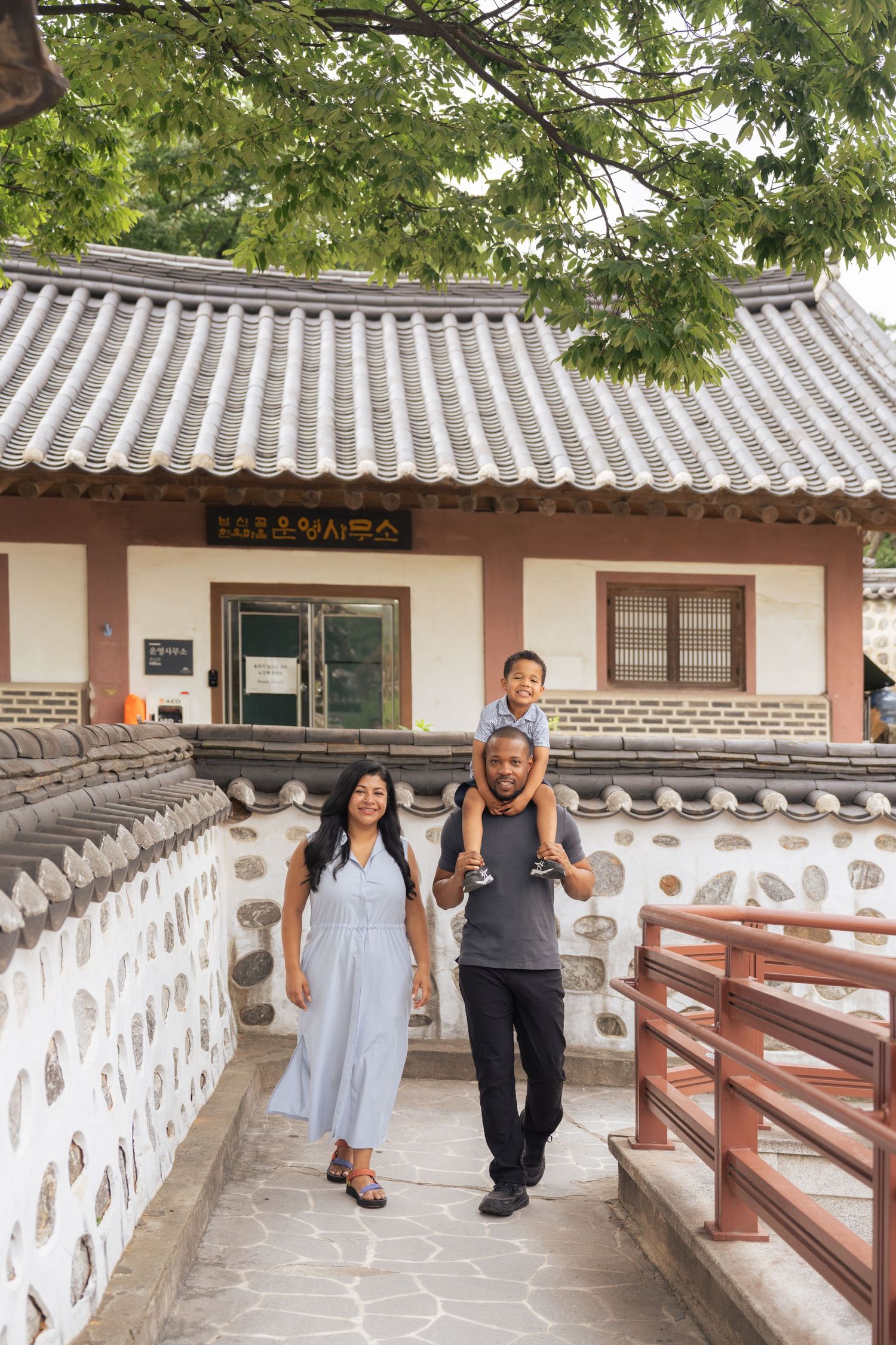 Couple walking along a traditional Korean architectural corridor with white stone walls and wooden beams in summer.