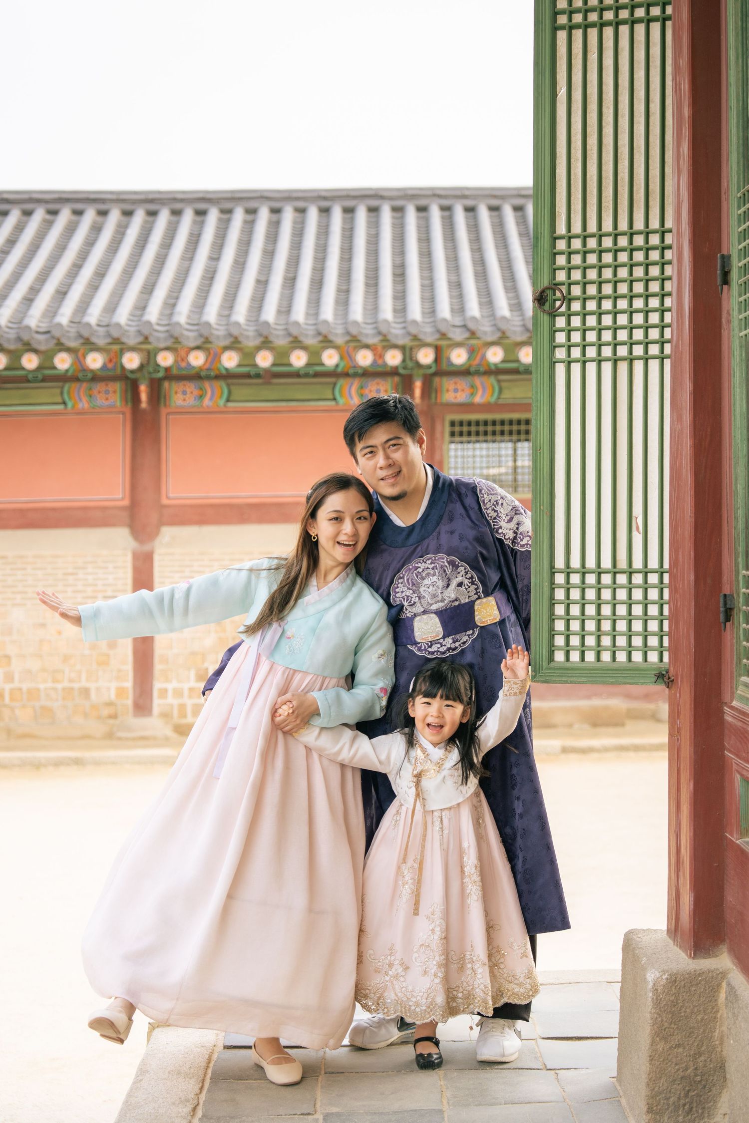 A family wearing traditional Korean hanbok attire poses together in a historic palace corridor.