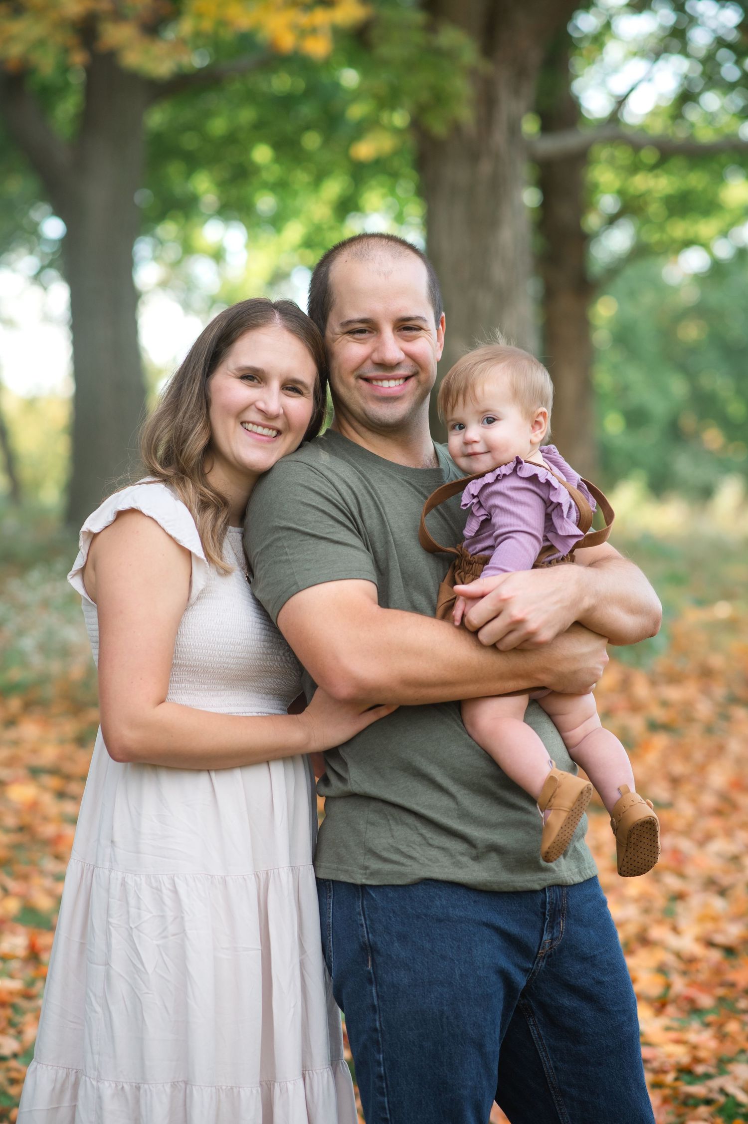 A happy family laughs together outdoors on a sunny day with pink flowering trees in the background.