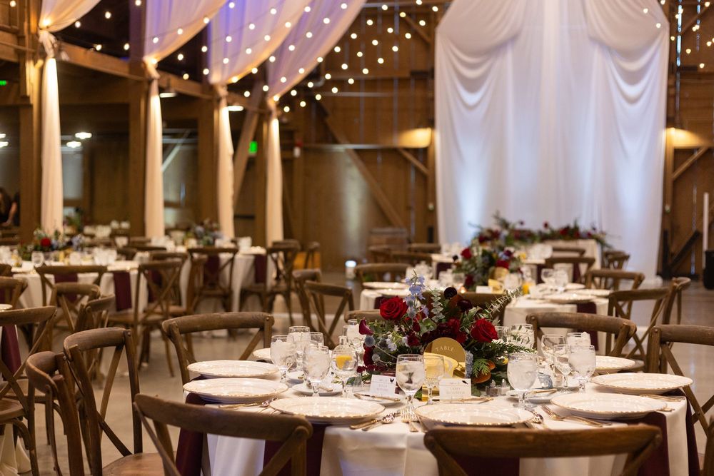 Elegant wedding reception venue with round tables, wooden chairs, and twinkling string lights overhead.