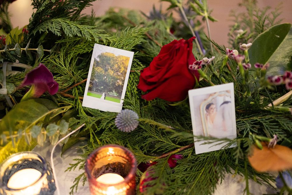 Wedding table centerpiece featuring evergreen branches, red roses, and vintage photographs.