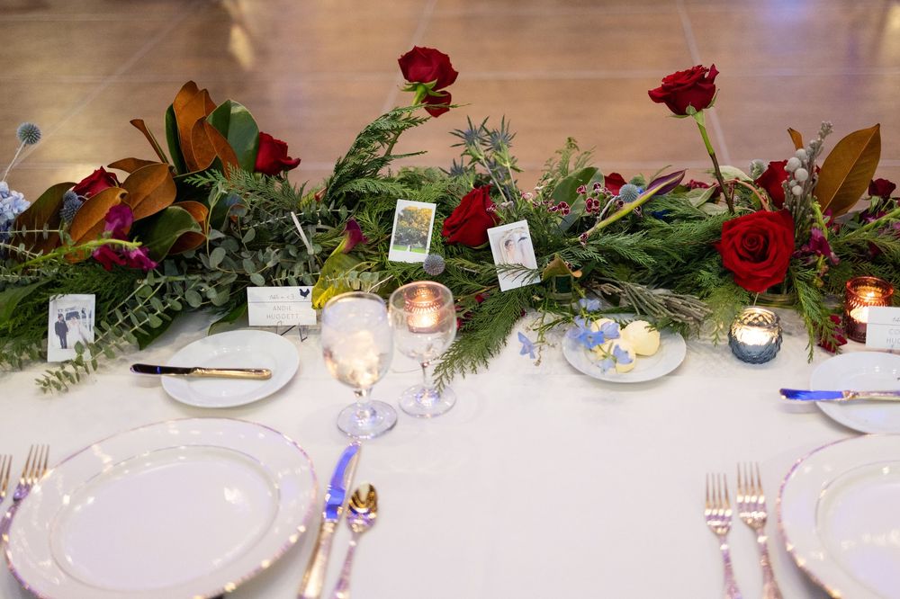 Elegant wedding reception table decorated with red roses, greenery, and glowing candles in a rustic setting.