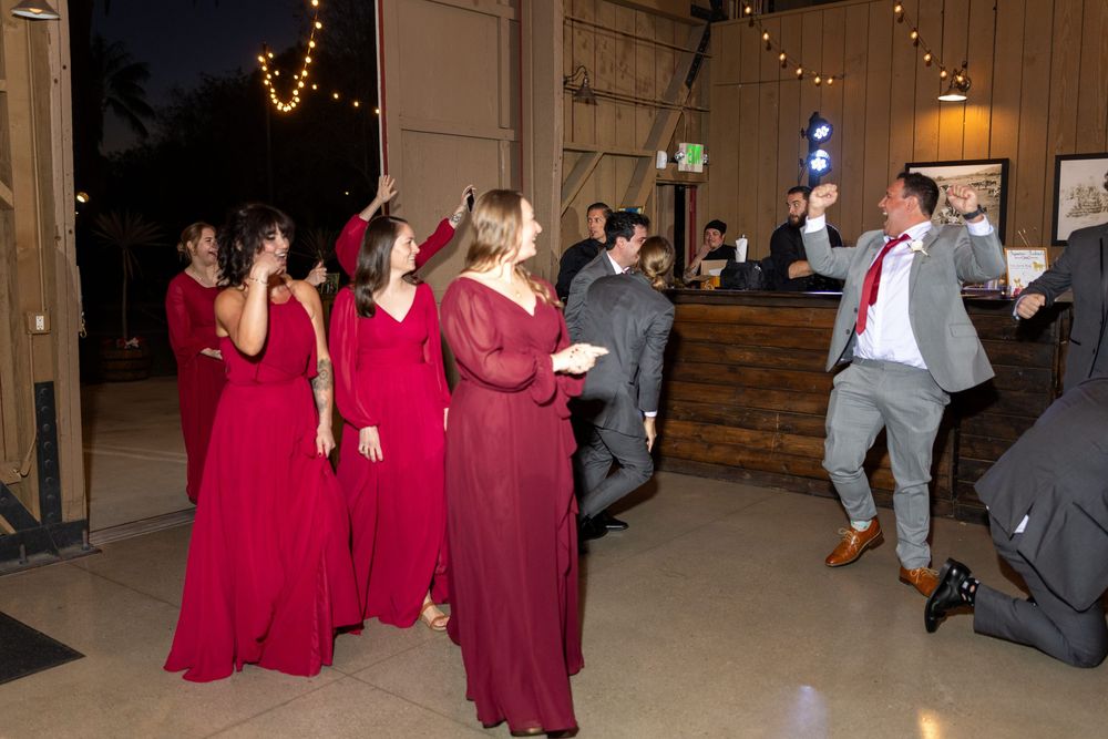 Wedding guests dancing and celebrating on a dance floor decorated with string lights and rustic wooden details.