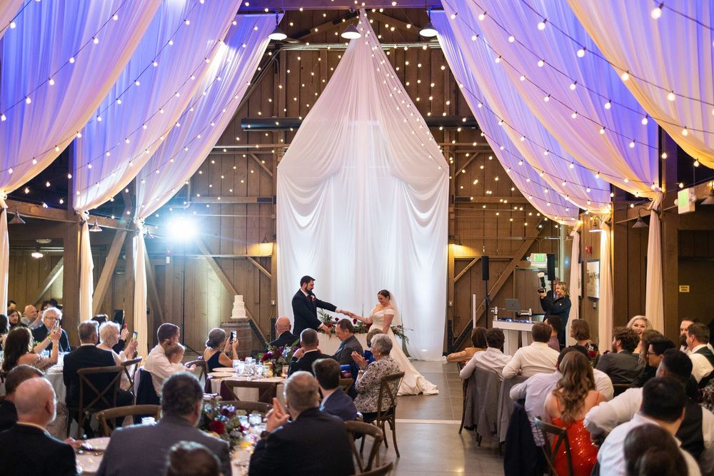 Wedding reception venue decorated with elegant white draping, string lights and purple uplighting creating romantic ambiance.