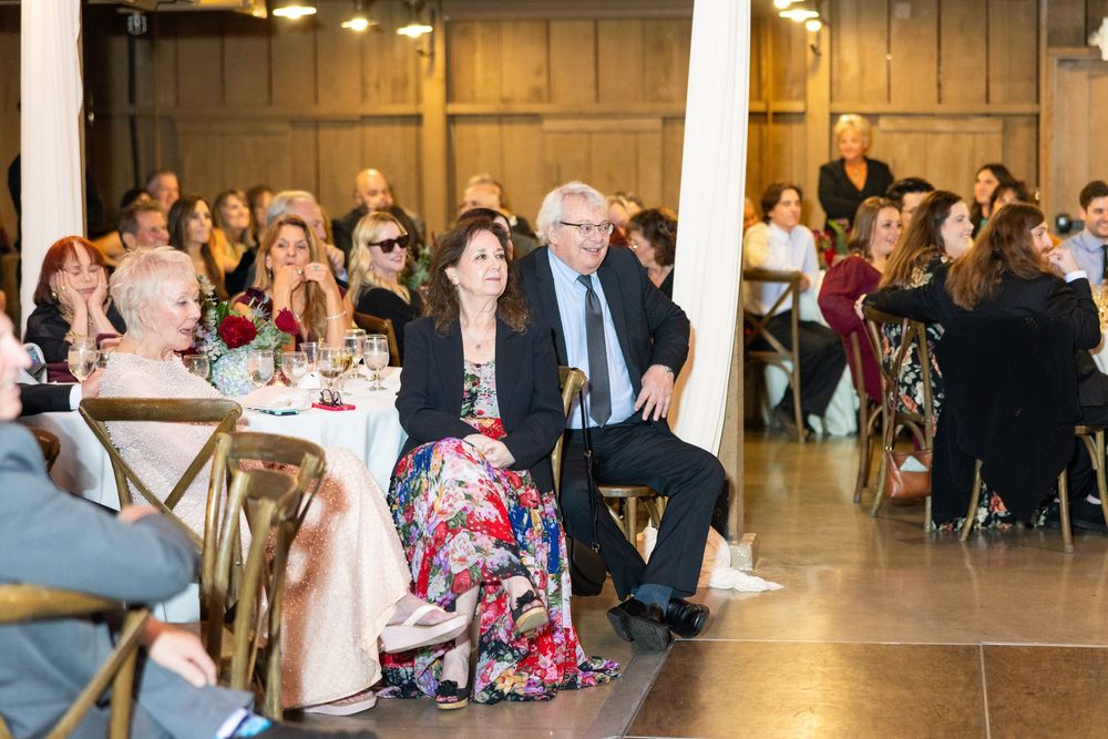 Wedding guests seated at tables in a rustic barn venue decorated with white drapes and elegant lighting.