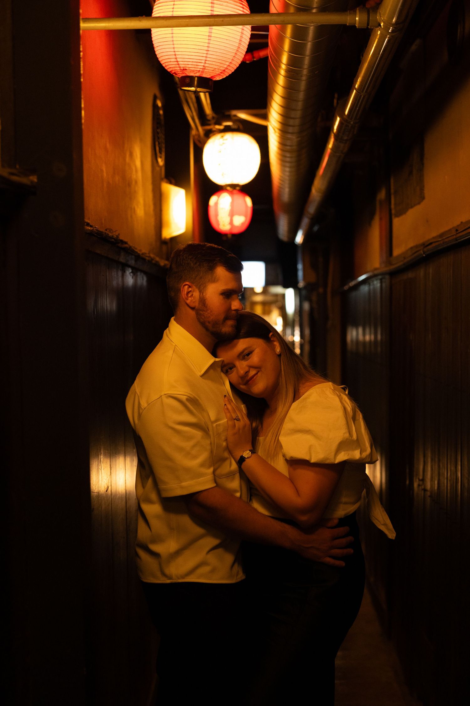 Couple sharing a tender moment in a cozy lantern-lit Japanese alleyway at night.