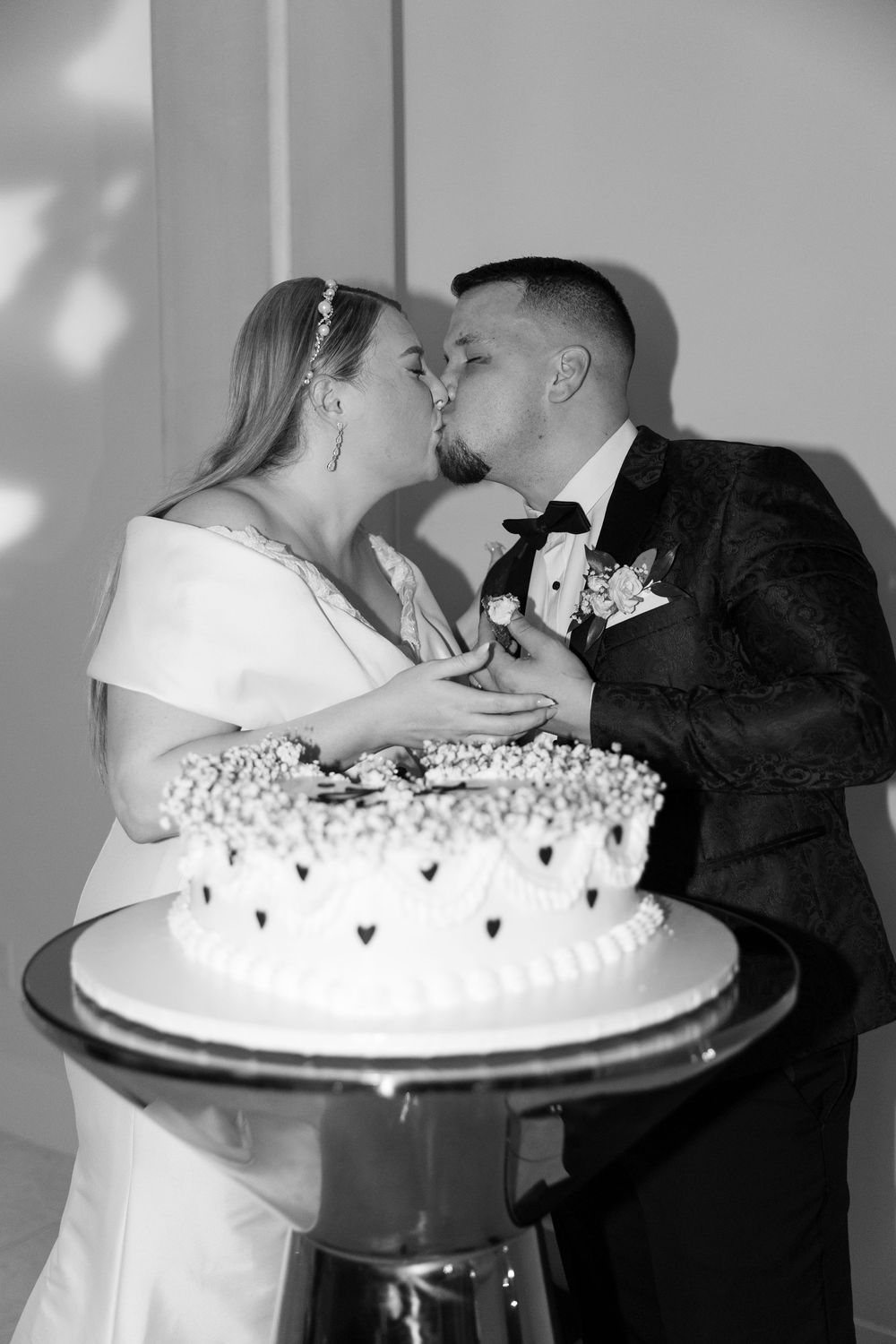 A romantic cake-cutting moment captured in black and white at a wedding reception.