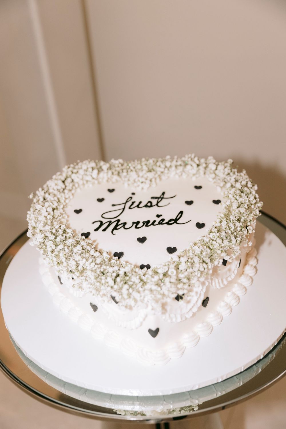A white wedding cake decorated with small hearts and 'Just Married' text surrounded by delicate frosting details.