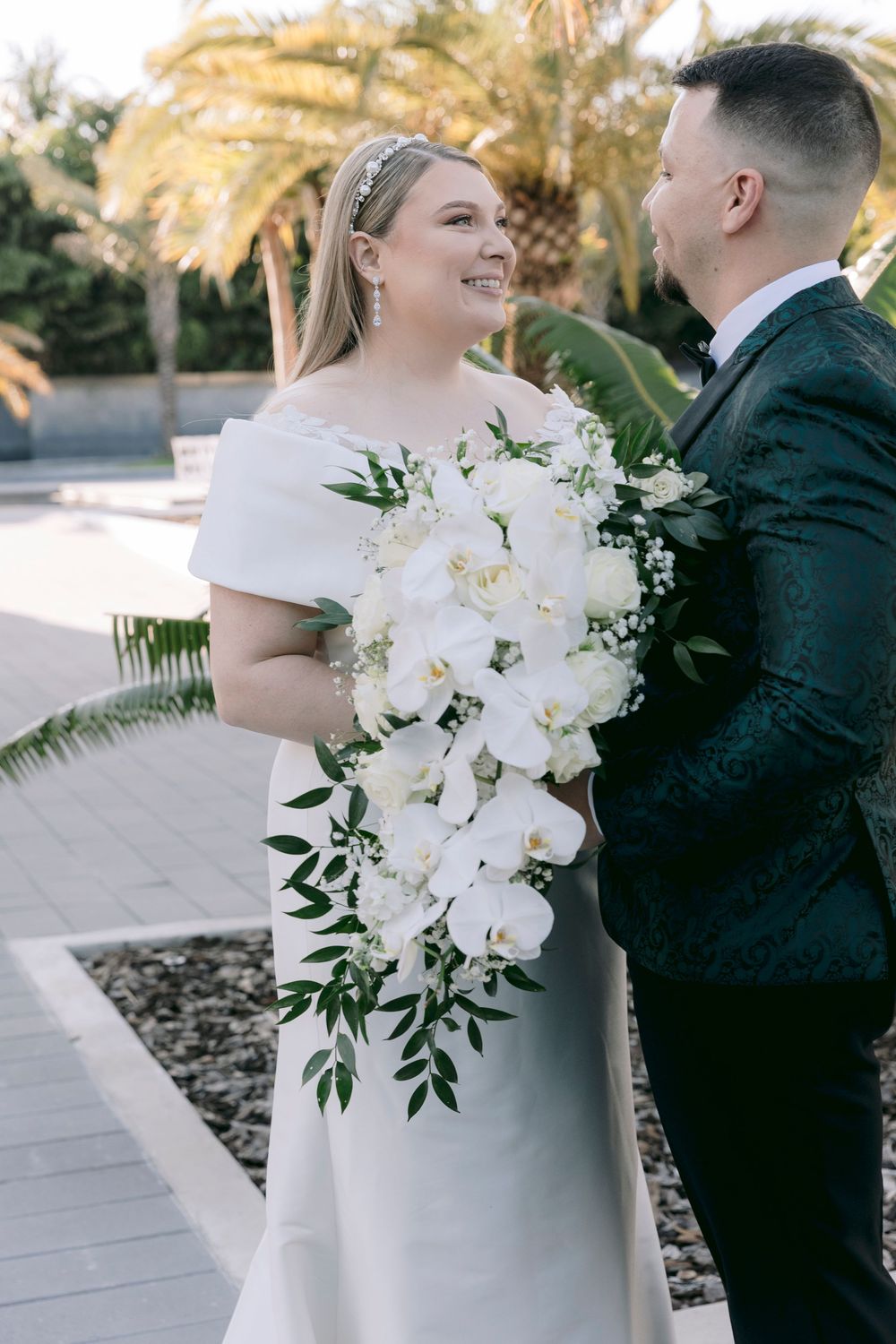 Elegant white orchid wedding bouquet held against tropical palm background.