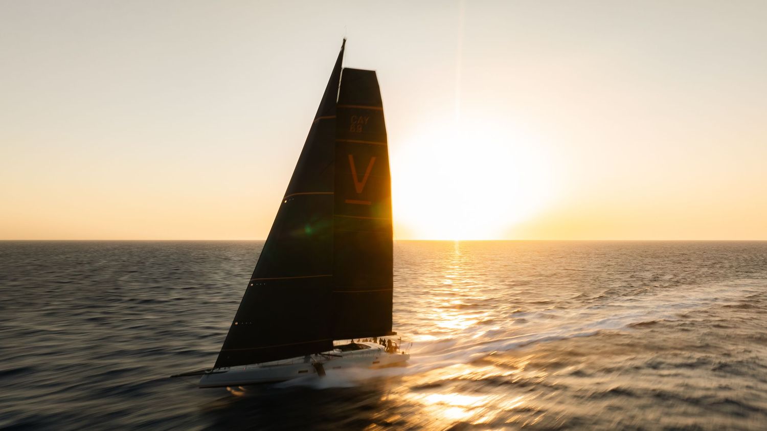 Sailboat silhouetted against golden sunset over calm ocean waters.