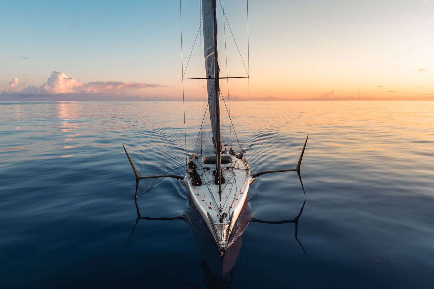 Aerial view of sailboat on calm ocean waters during peaceful sunset.