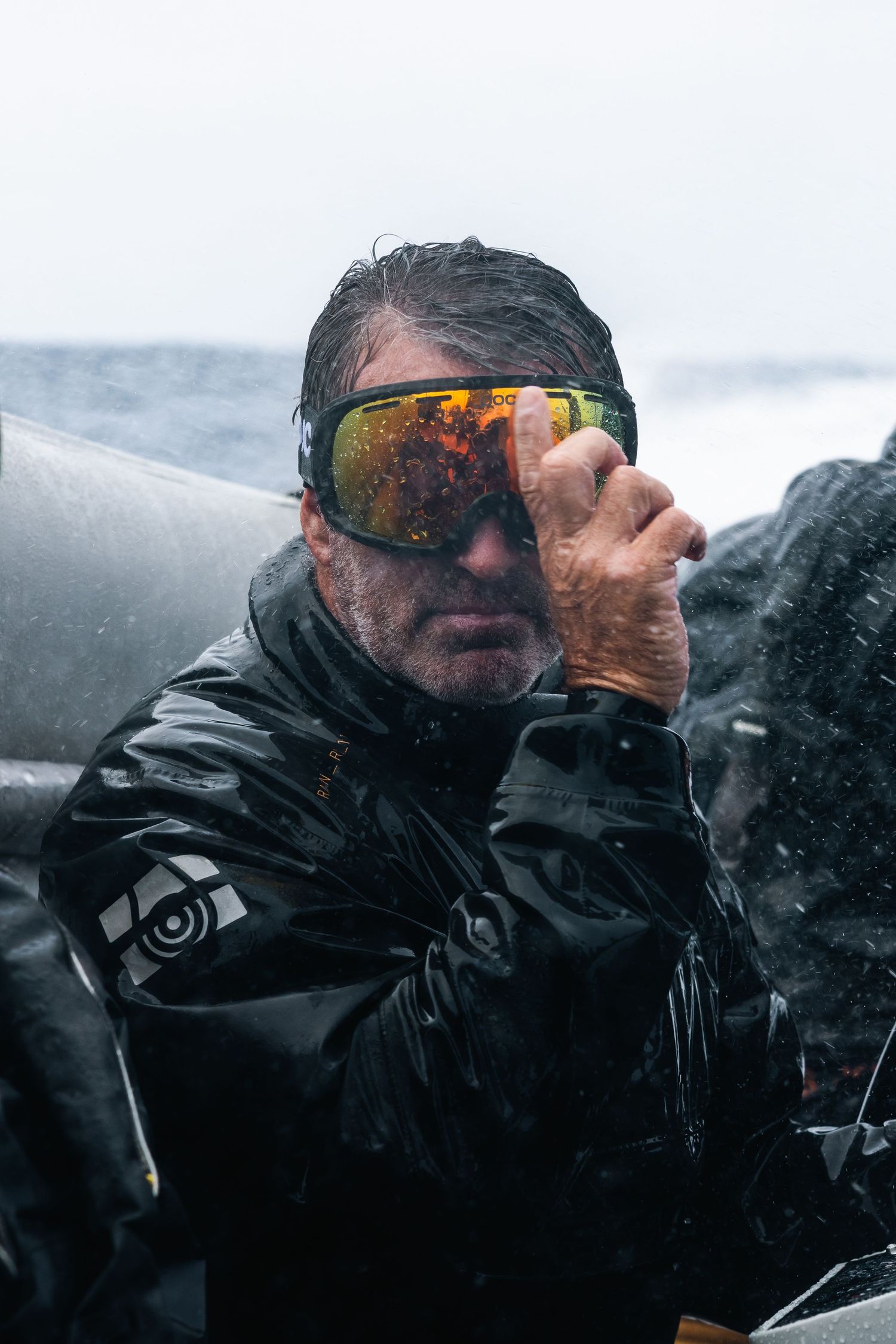 Sailor wearing reflective sunglasses and waterproof gear in stormy conditions at sea.