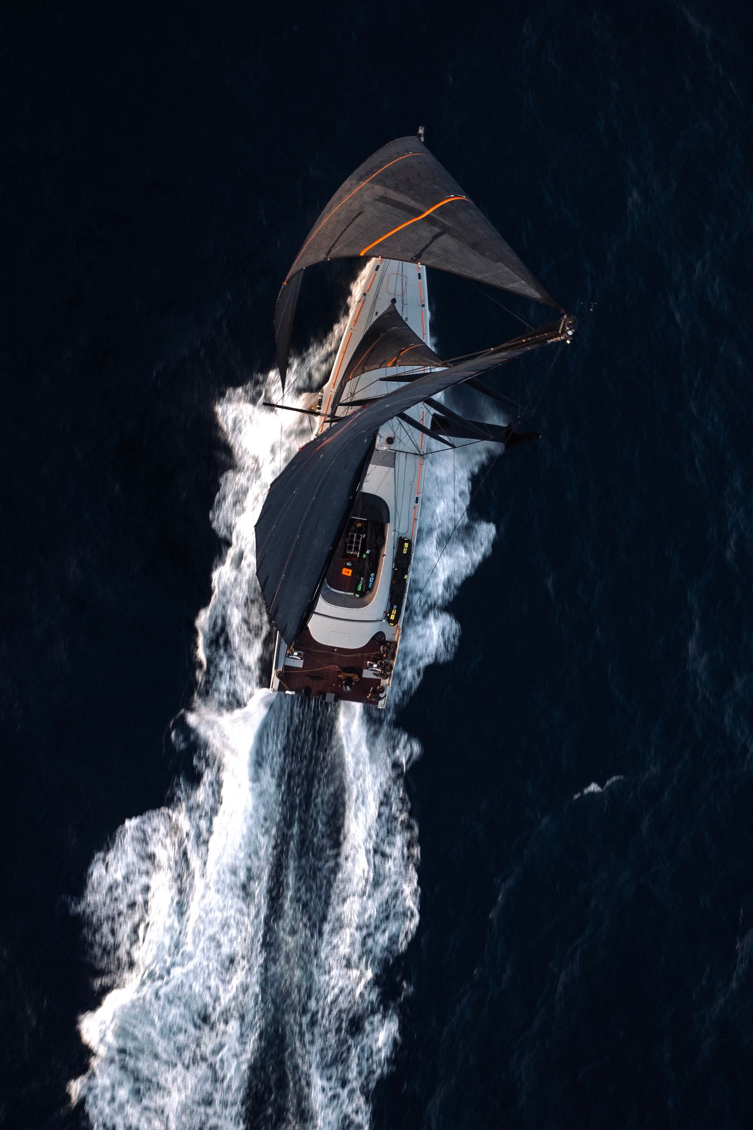 Aerial view of luxury sailing yacht creating white wake pattern in dark ocean waters.