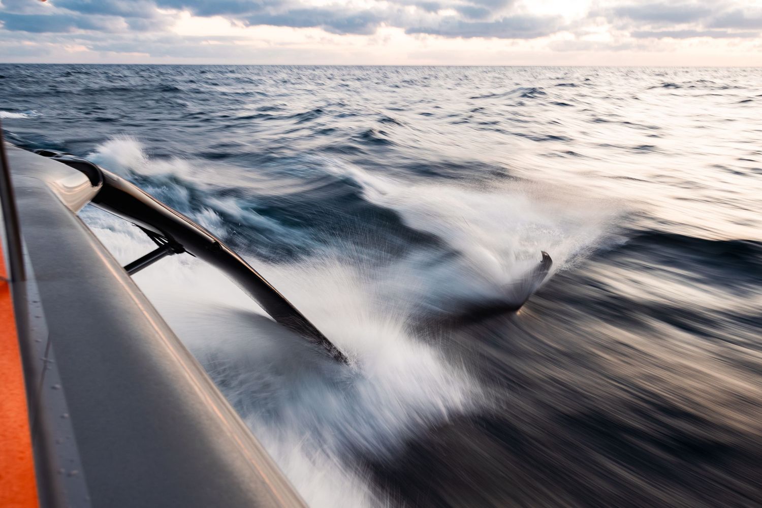 Ocean spray and waves crash against the side of a racing yacht at sea.