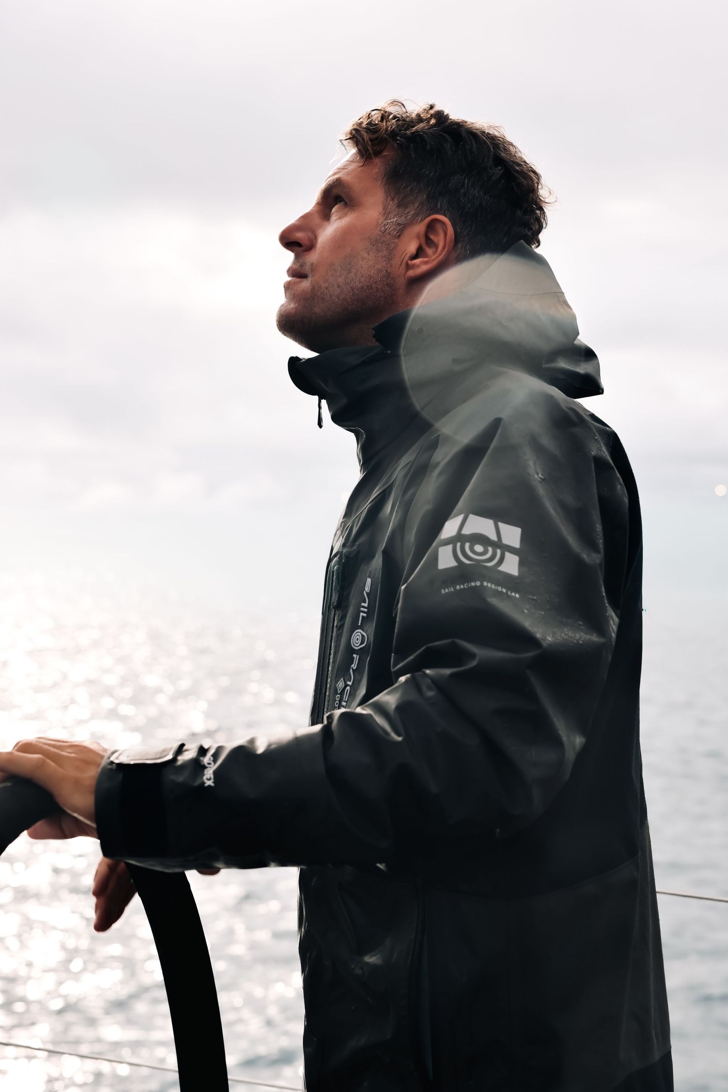 Person in a dark rain jacket stands against an overcast sky while fishing near a body of water.