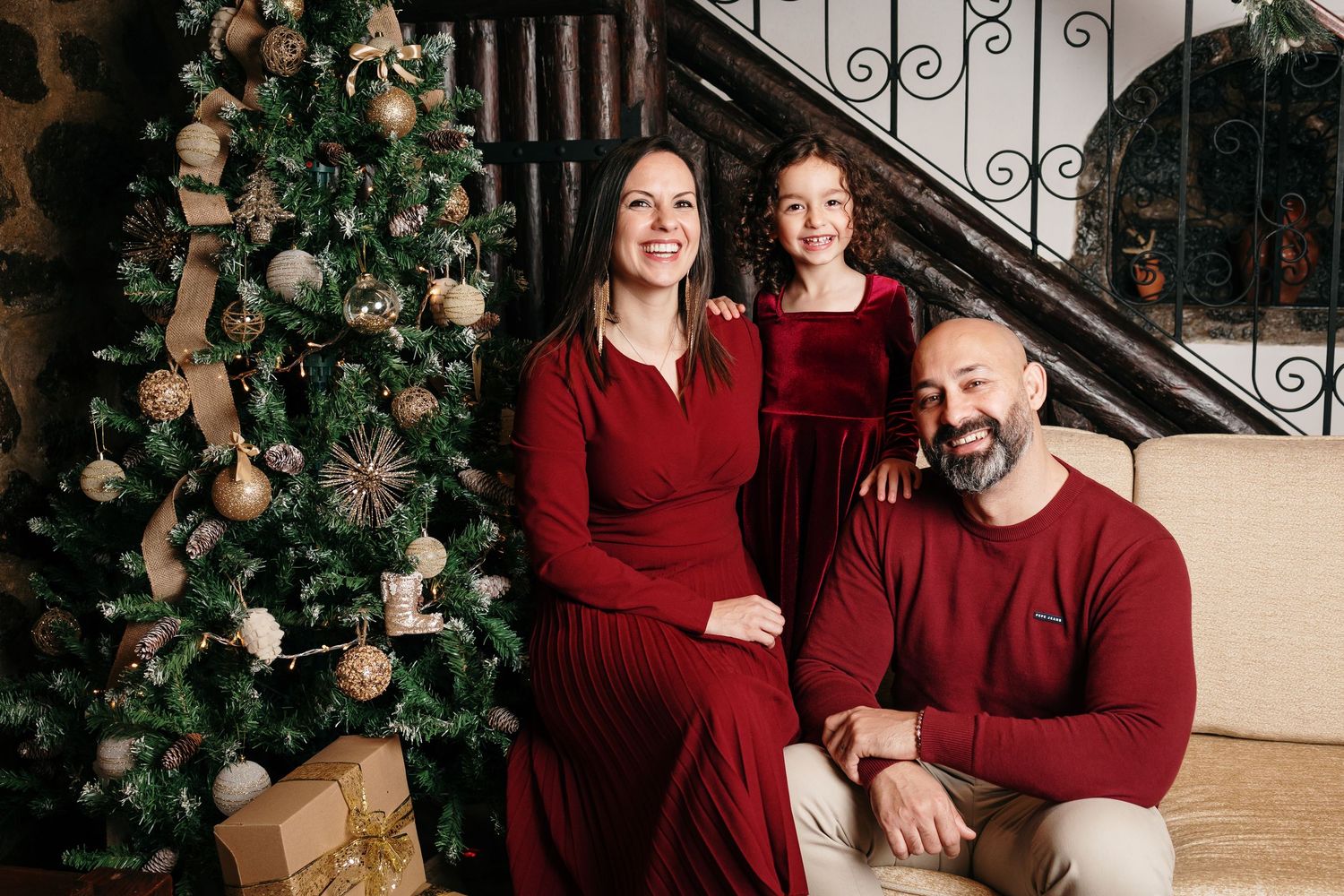 Family wearing coordinating burgundy outfits posed together near decorated Christmas tree.