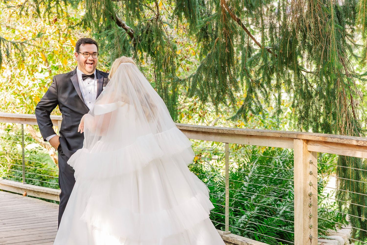 A wedding couple shares a romantic moment under sunlit trees in an outdoor garden setting.