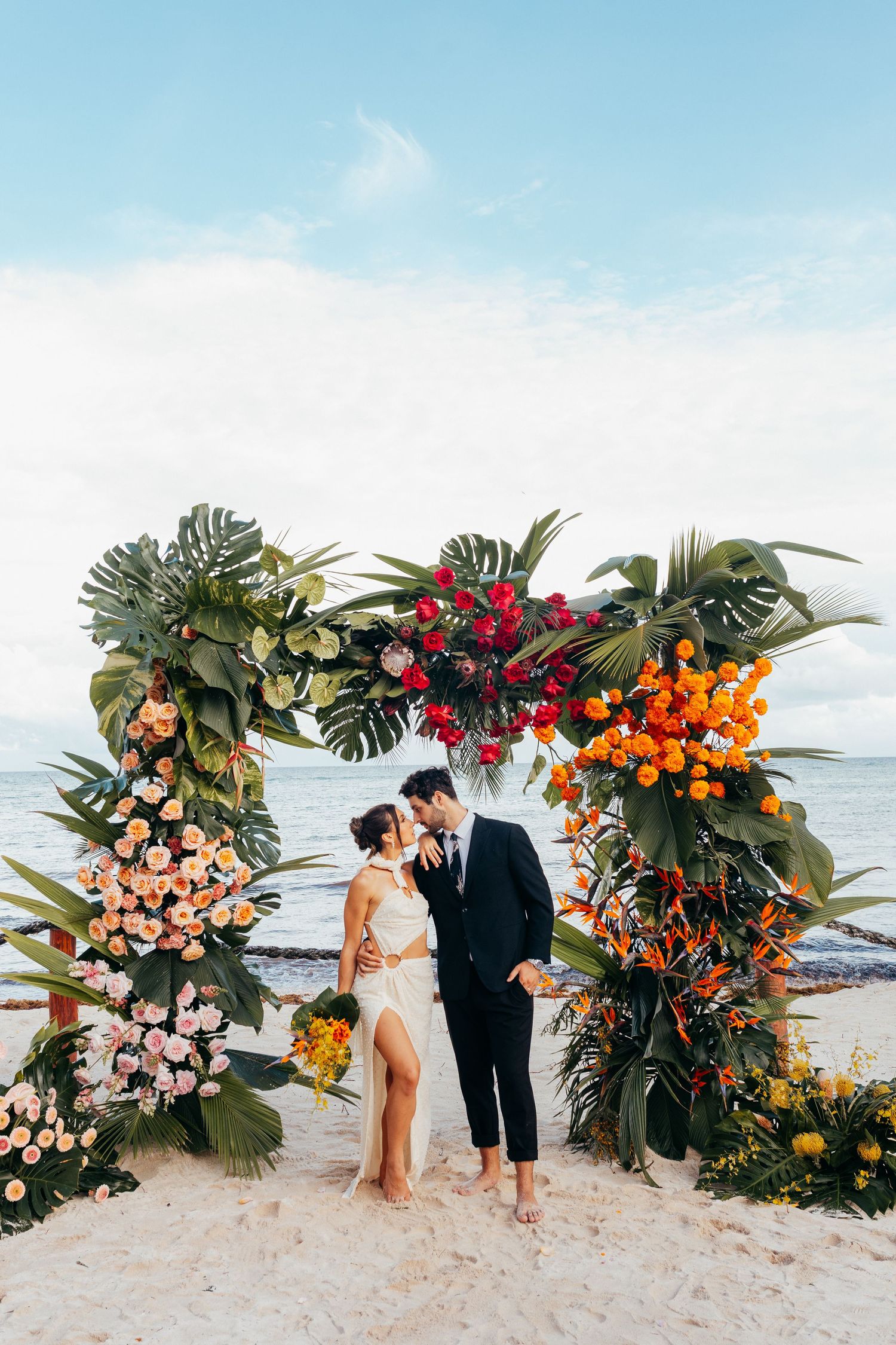 Wedding party poses together on a tropical beach with palm trees swaying in the breeze at sunset.