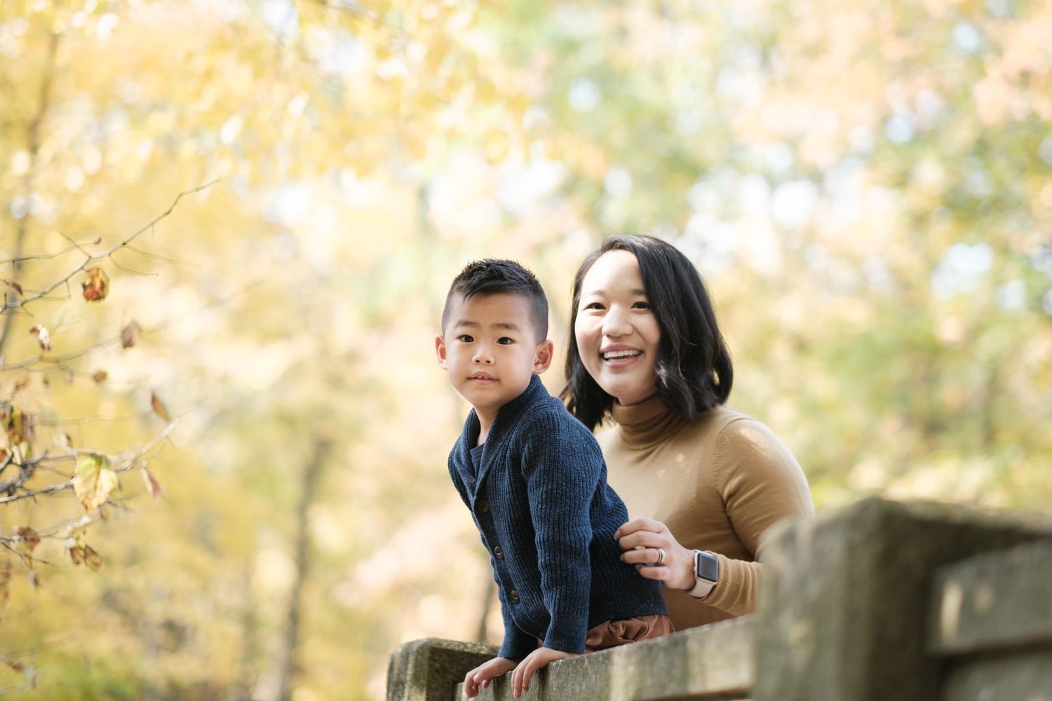 Family enjoying a playful autumn photoshoot outdoors with golden yellow foliage in the background.